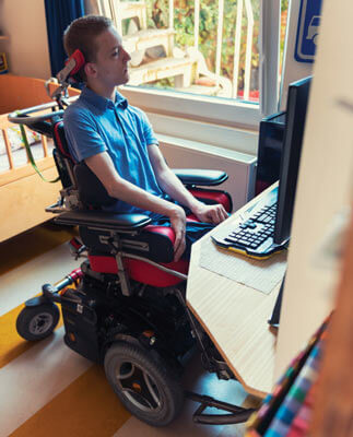 A man using a power wheelchair at his computer